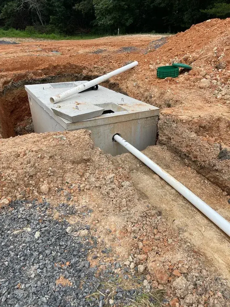 Concrete septic tank set in the ground with PVC inlet and outlet pipes and green riser lids nearby