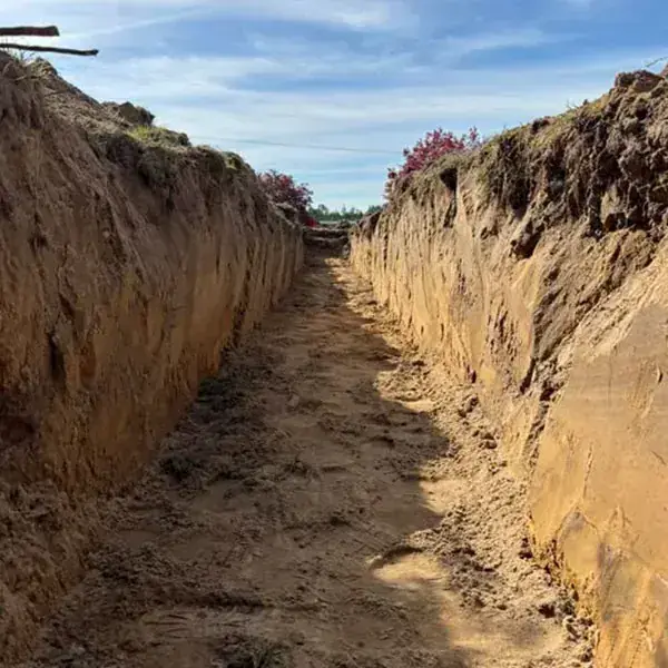 Deep narrow trench cut into sandy clay soil showing the layers a soil evaluation reads