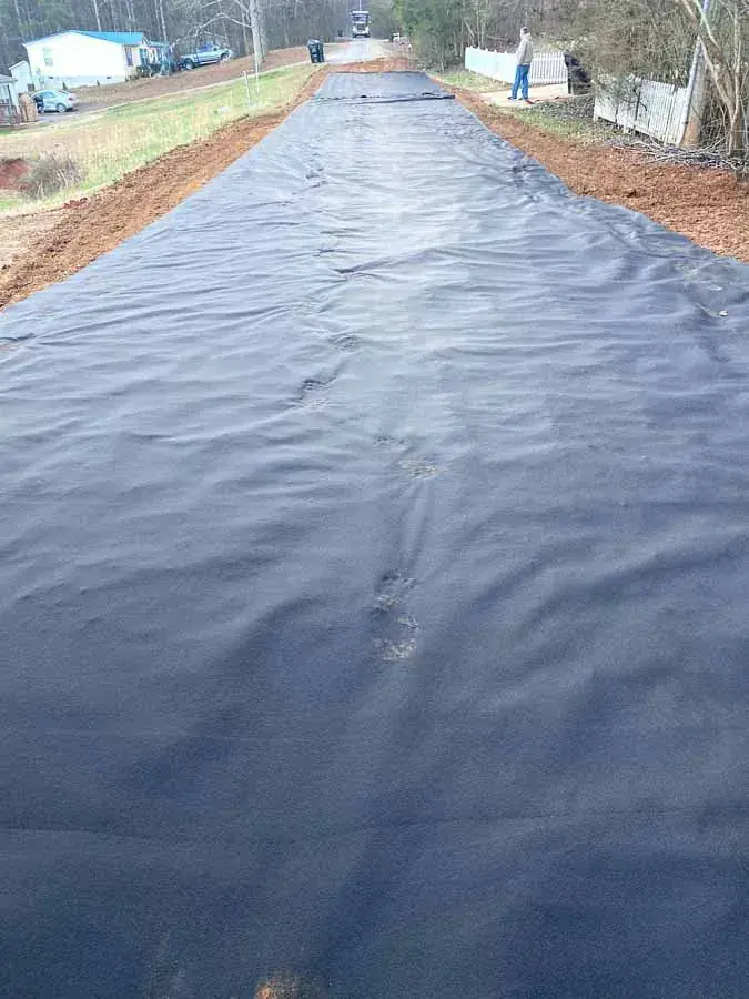 Black geotextile fabric spread over a long graded septic field area beside a rural road