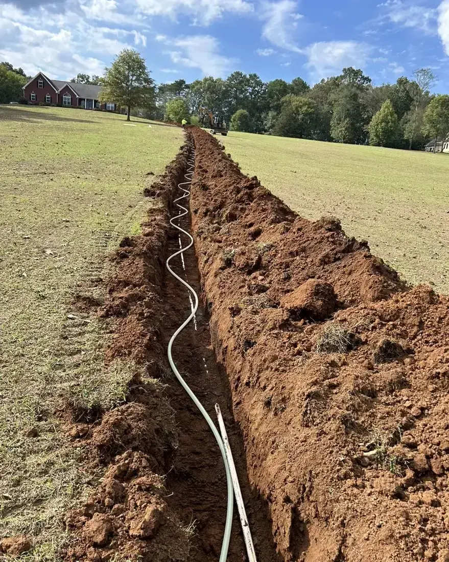 Long open trench across a lawn with a flexible pipe snaking along the bottom