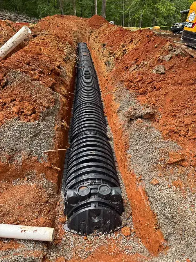 Black plastic drain field chambers laid end to end in a deep red clay trench