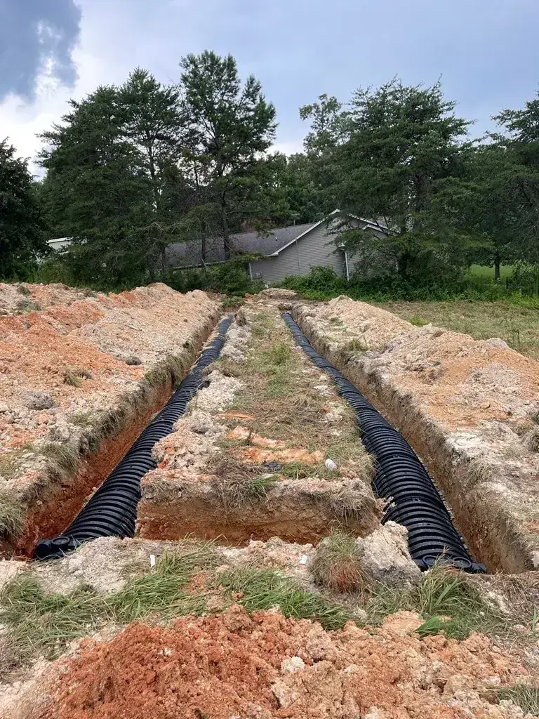Two parallel drain field trenches with black chambers installed and a gray house behind