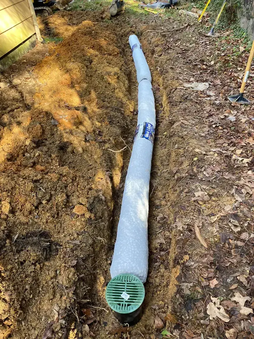 Fabric wrapped drain pipe in a trench ending at a green catch basin grate